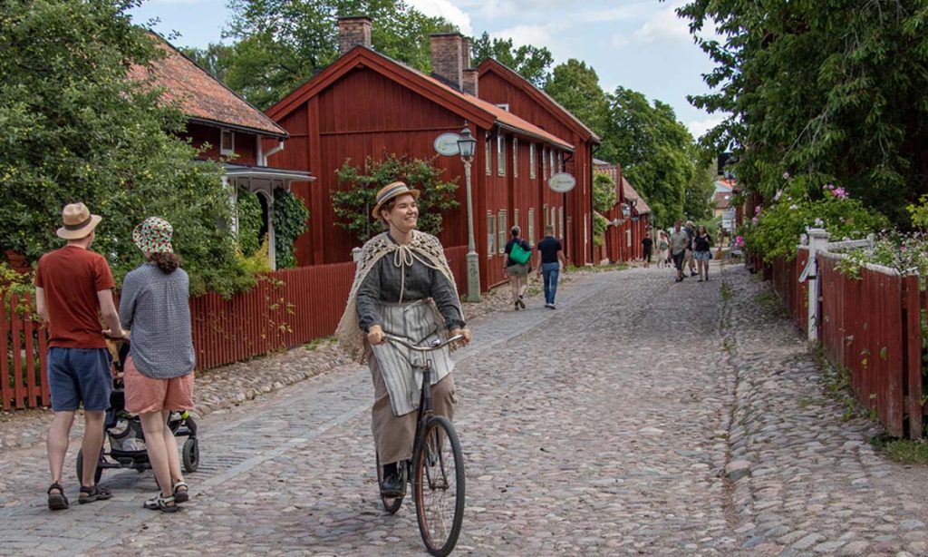 "Frau in Kleidung aus dem 19. Jahrhundert, die in Gamla Linköping Fahrrad fährt.
